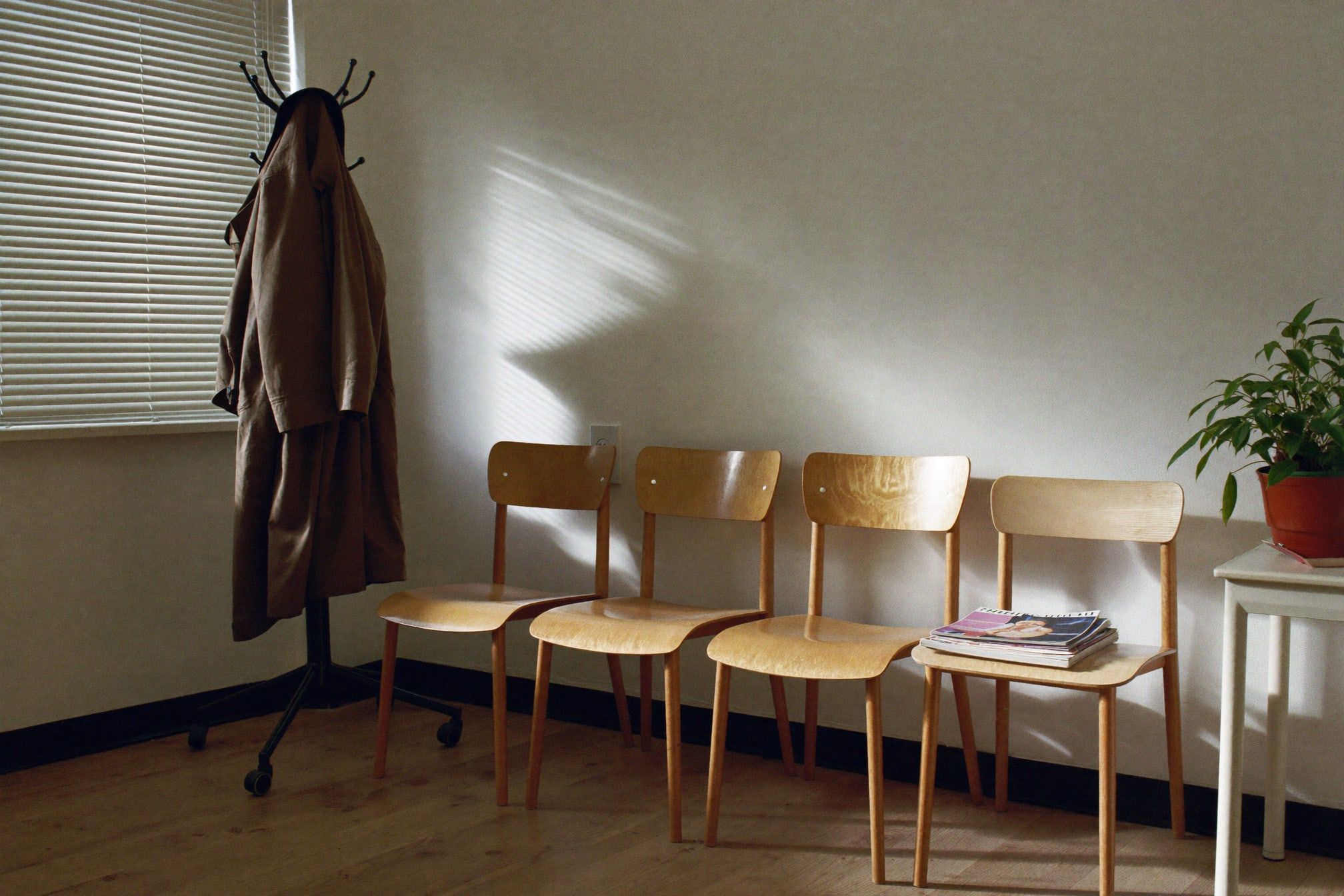 Ruhiges Wartezimmer einer Hausarztpraxis mit vier Holzstühlen und Garderobe